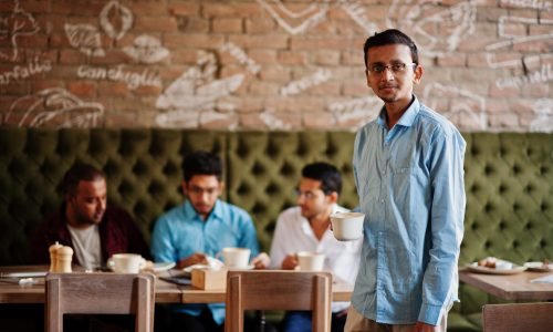 Group of four south asian men's posed at business meeting in cafe. Indians work together, having conversation. Indian man with cup of coffee.